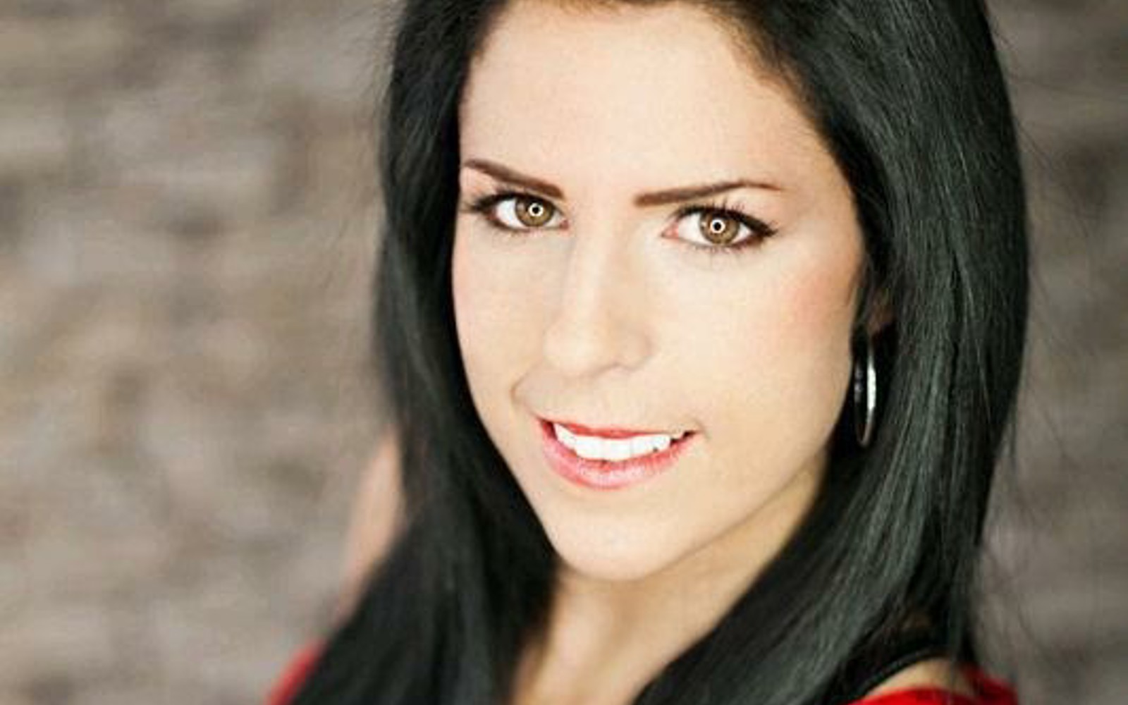 Portrait d'une femme aux longs cheveux bruns vêtue d'un chemisier rouge sans manches.