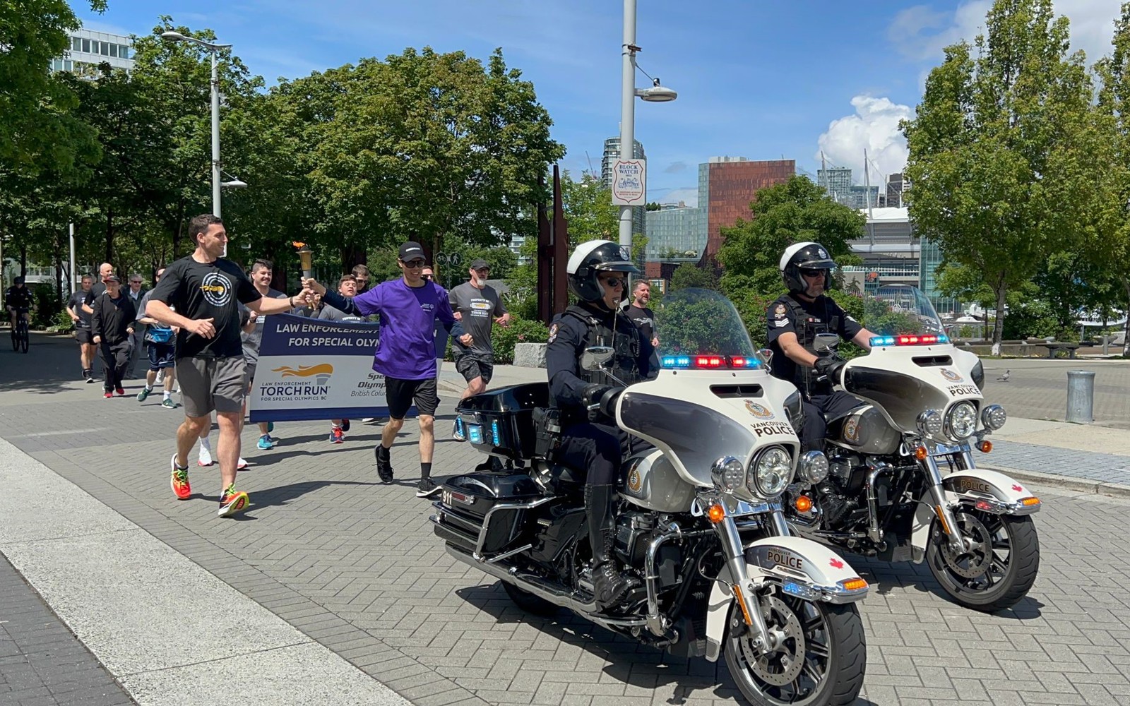 Participants run behind a police escort by two motorcycle officers while carrying the Law Enforcement Torch Run flame.