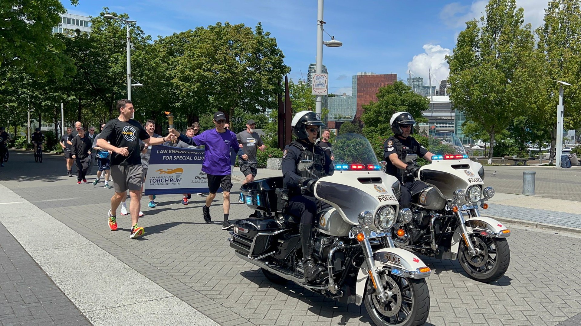 Participants run behind a police escort by two motorcycle officers while carrying the Law Enforcement Torch Run flame.