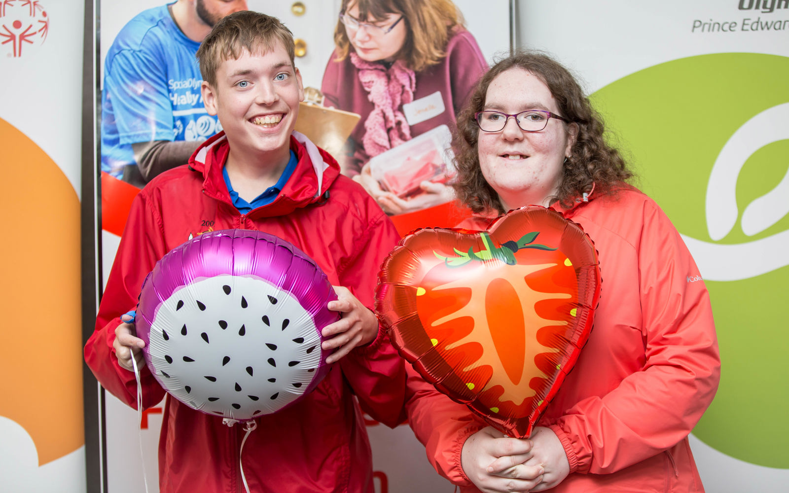 Twp people smile at the camera while holding ballons.