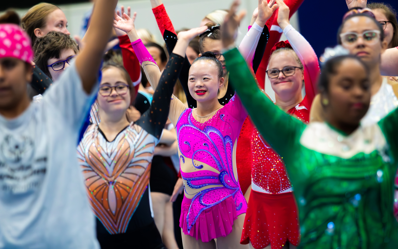 Groupe d'athlètes les bras levés. Tous sont souriants et portent des costumes de patinage artistique