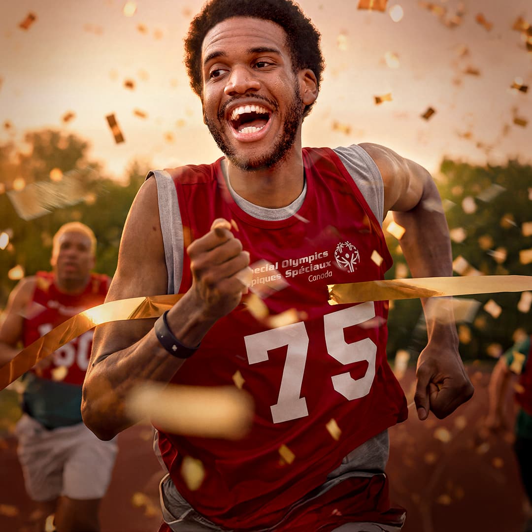 Man in a red special olympics shirt running while gold confetti falls around him 