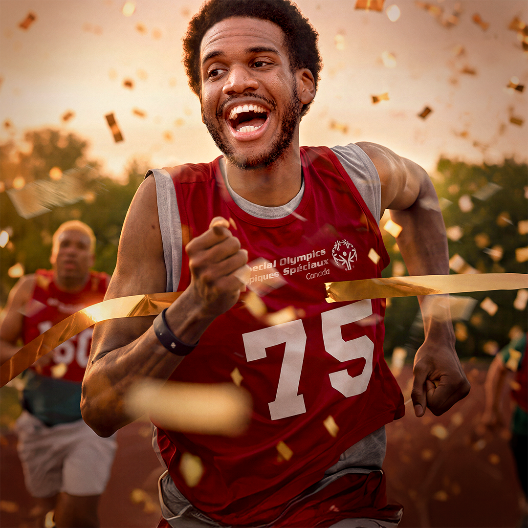 Man in a red special olympics shirt running while gold confetti falls around him Man in a red special olympics shirt running while gold confetti falls around him