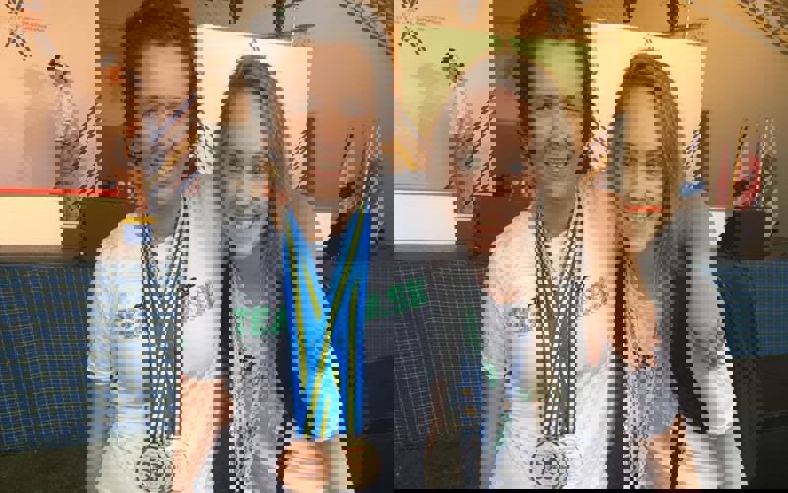 A photo of a volunteer and athlete with their arms around behind each other smiling for the camera. They are both wearing white t-shirts. The athlete has medals around her neck while the volunteer has a colourful lanyard around her neck.