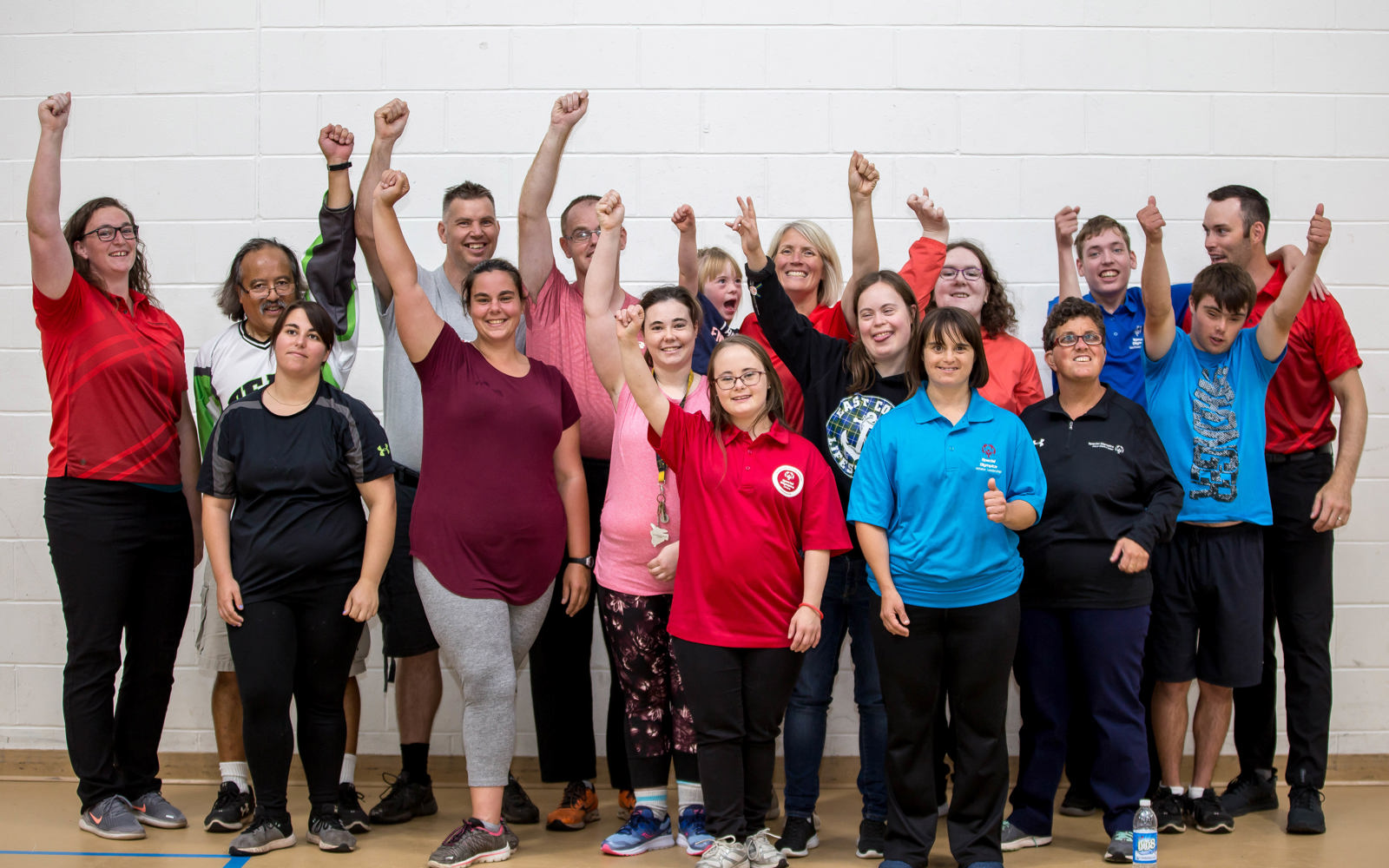 A group photo of athletes and volunteers smiling and raising their arms in celebration.