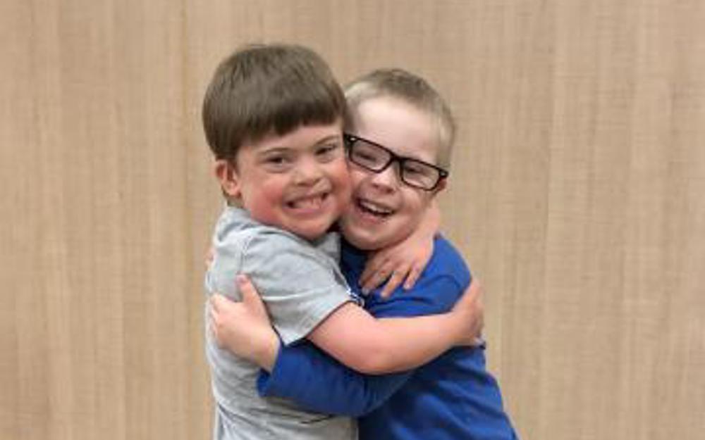 Two young athletes are hugging each other tightly and smiling for the camera.
