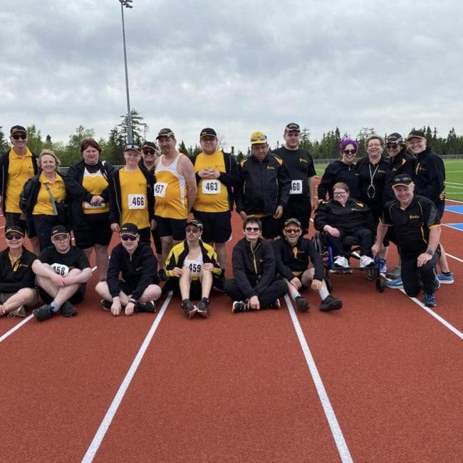 A group, team photo on the track. Everyone is in matching yellow and black team uniforms. The front row of people are sitting on the track while the back row of people are standing.