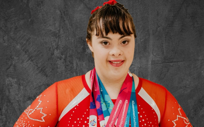 Rebecca wearing Special Olympics Team Canada 2023, Outfit posing with her hands on her hips witth 4 medals.