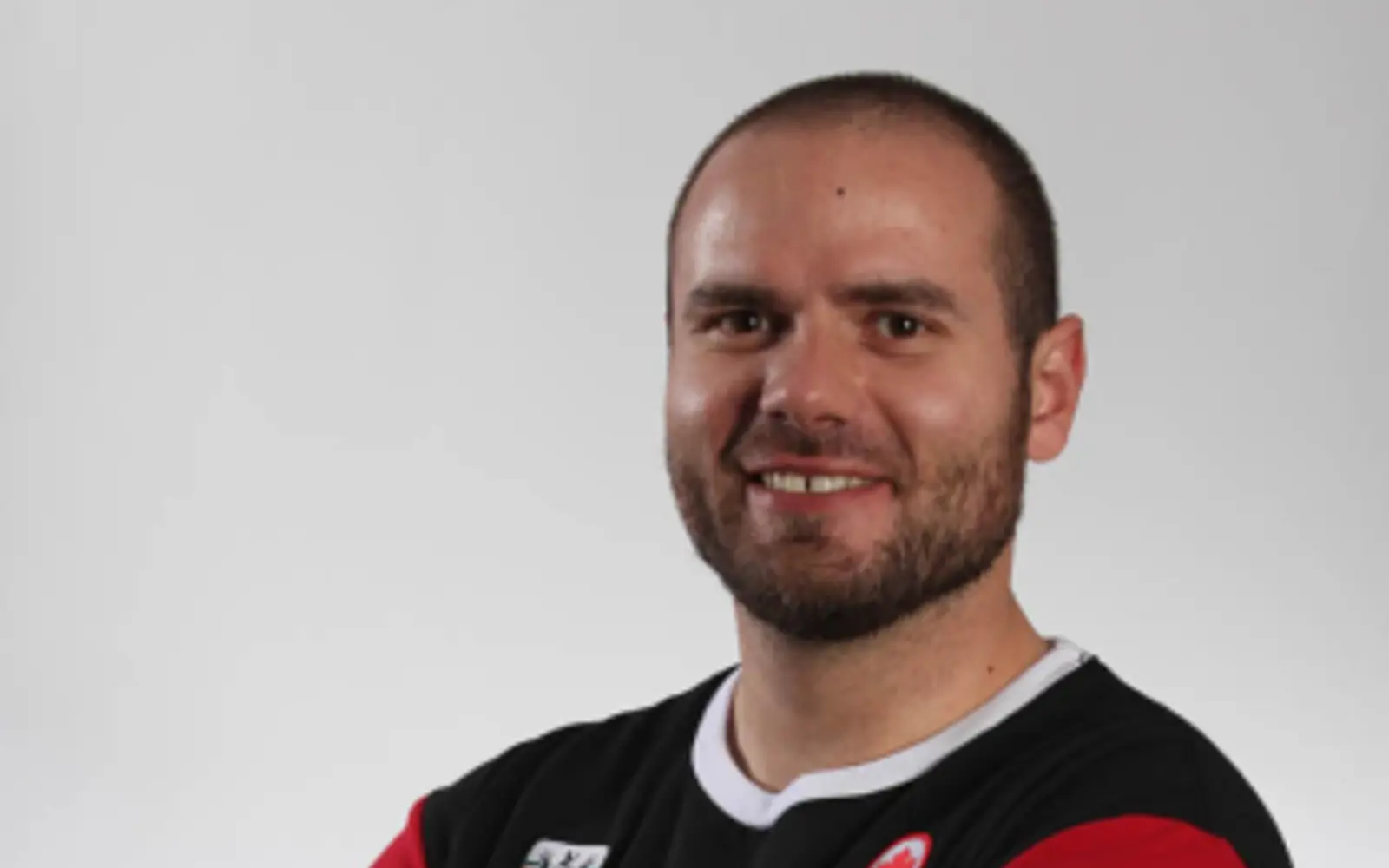 Portrait d'un homme les bras croisés, vêtu d'un t-shirt des Jeux olympiques du Canada.