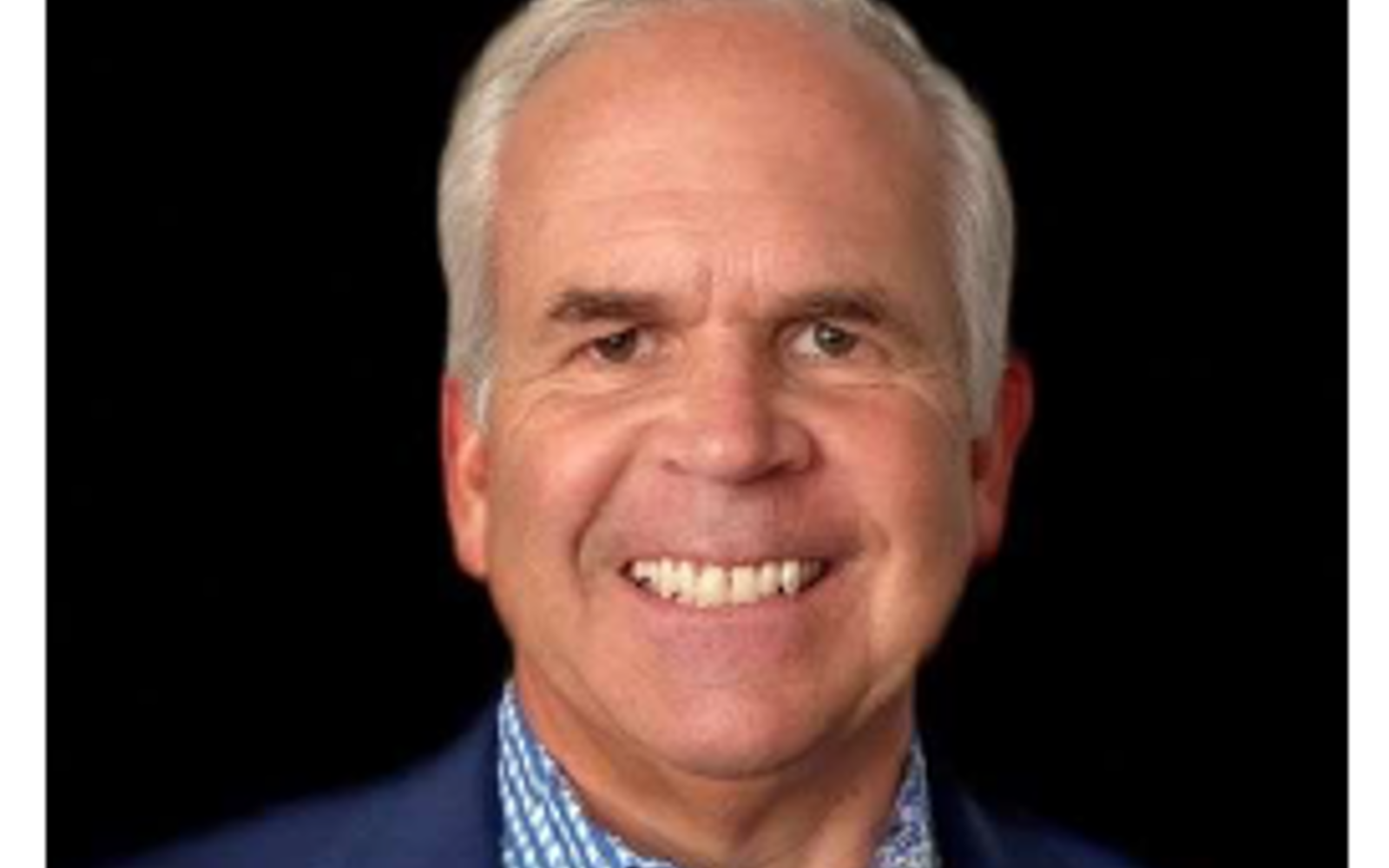 Man in blue sport coat and blue and white checked shirt  smiling at camera. 