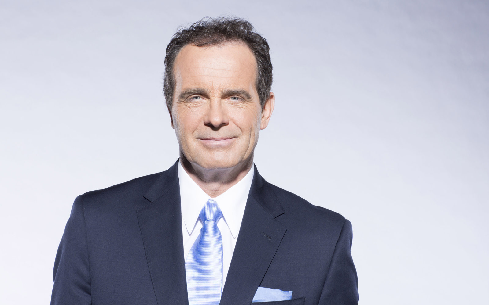 Portrait d'un homme aux cheveux foncés, vêtu d'un costume bleu, d'une chemise blanche et d'une cravate bleue.