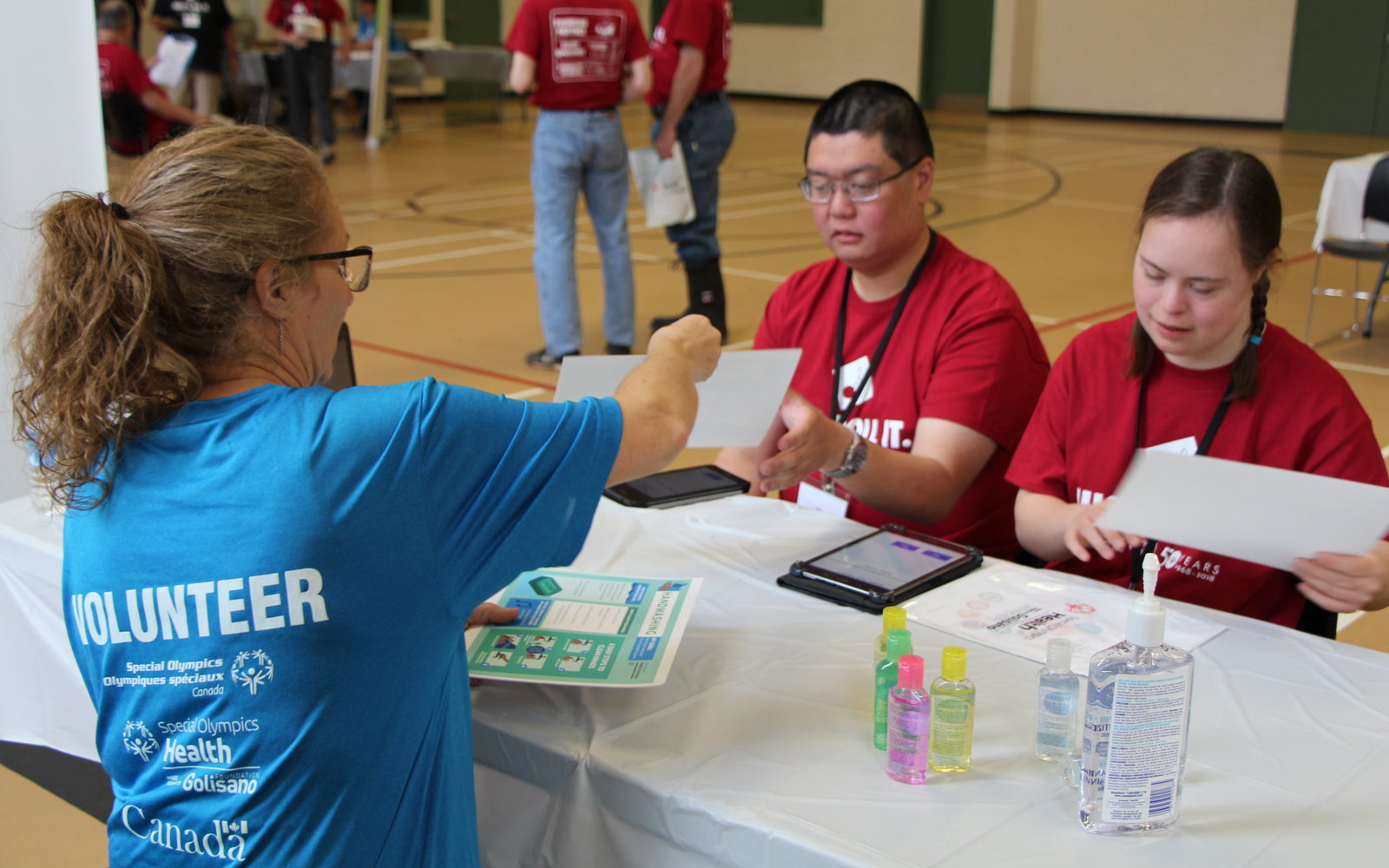 a person in a blue shirt talks to two athletes in red shirts.