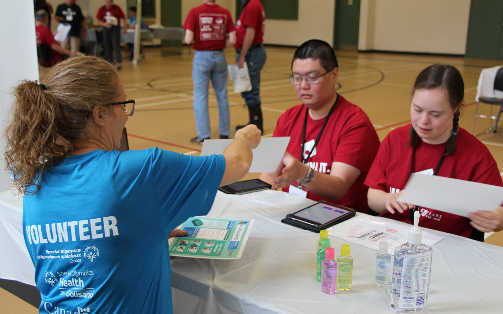 a person in a blue shirt talks to two athletes in red shirts. 