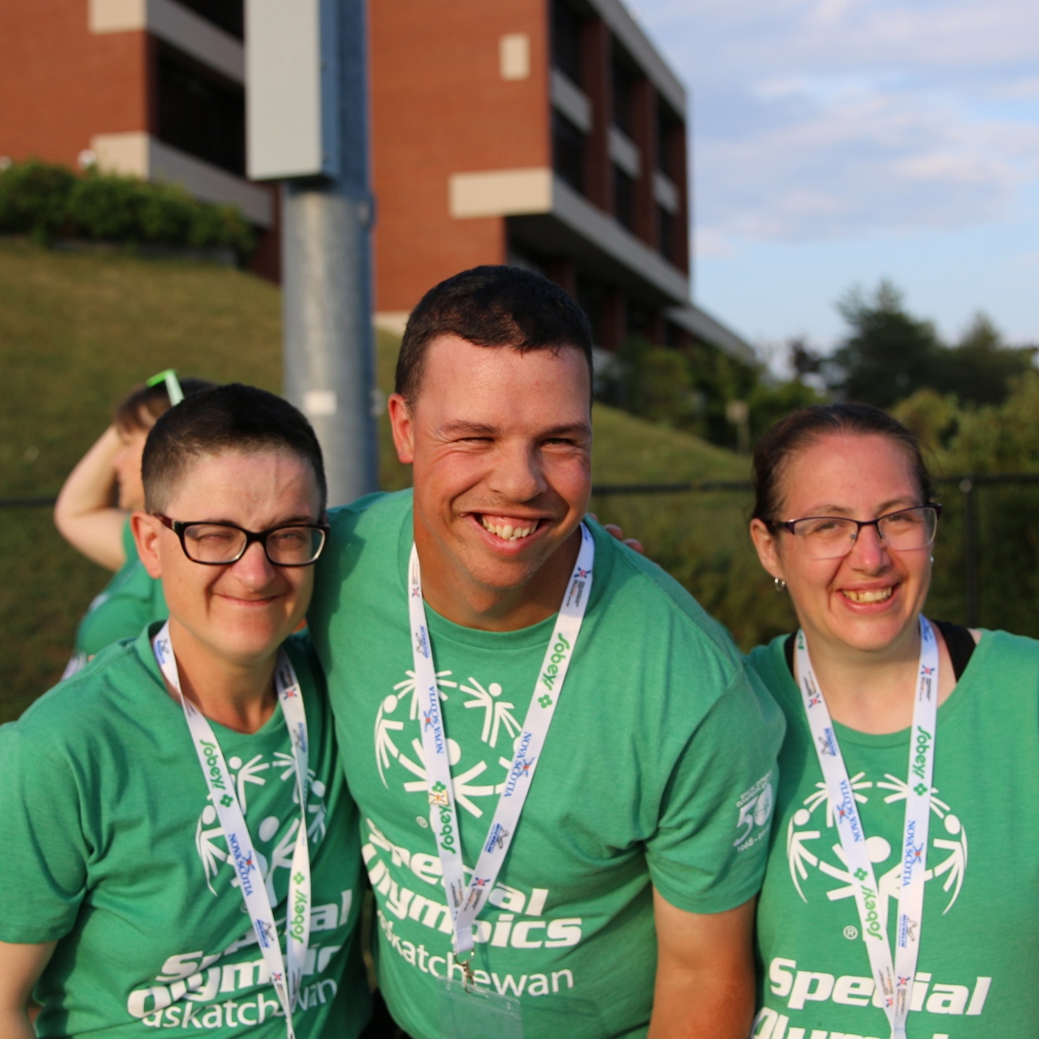 Three Special Olympics Saskatchewan athletes are smiling for the camera. They are all wearing green Special Olympics Saskatchewan t-shirts and white lanyards.