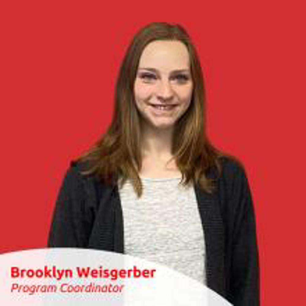 Portrait Photo of Brooklyn Weisgerber. She is standing against a red wall and smiling for the camera.