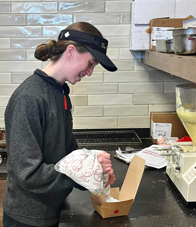 Women in a gray Tim Hortons shirt and hat is making a donut.