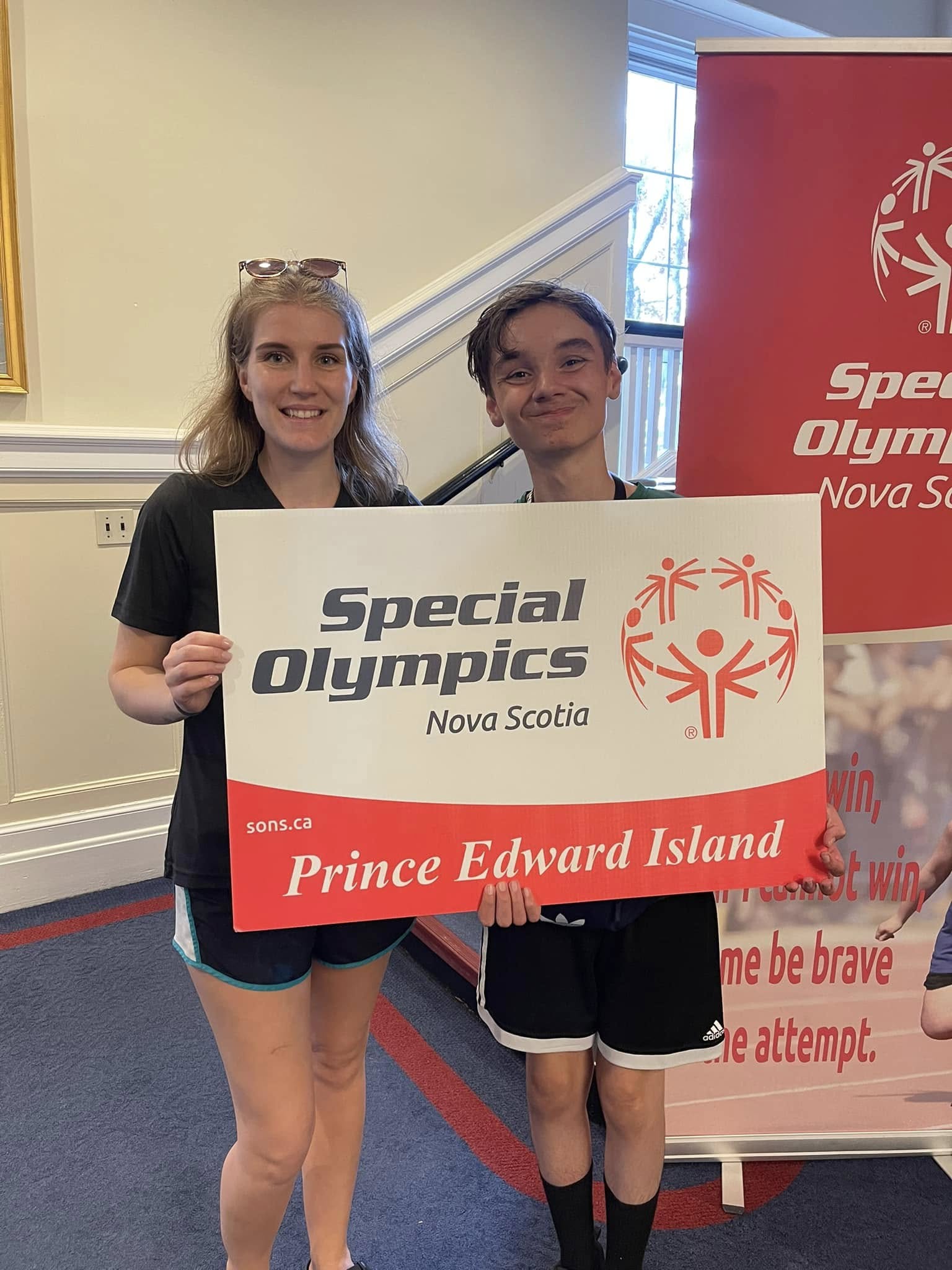 An athlete and a volunteer stand with a Special Olympics PEI sign