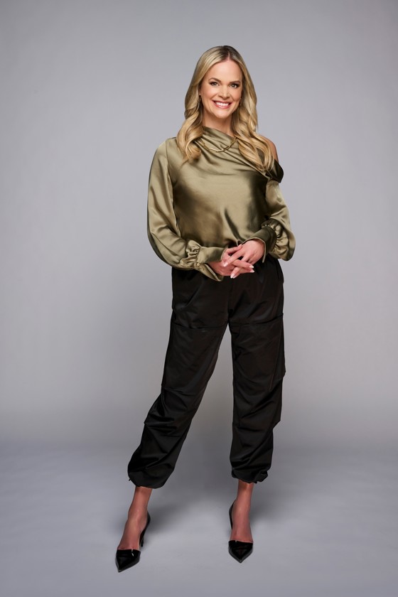 Portrait d'une femme aux longs cheveux blonds vêtue d'une chemise en soie verte et d'un pantalon noir.