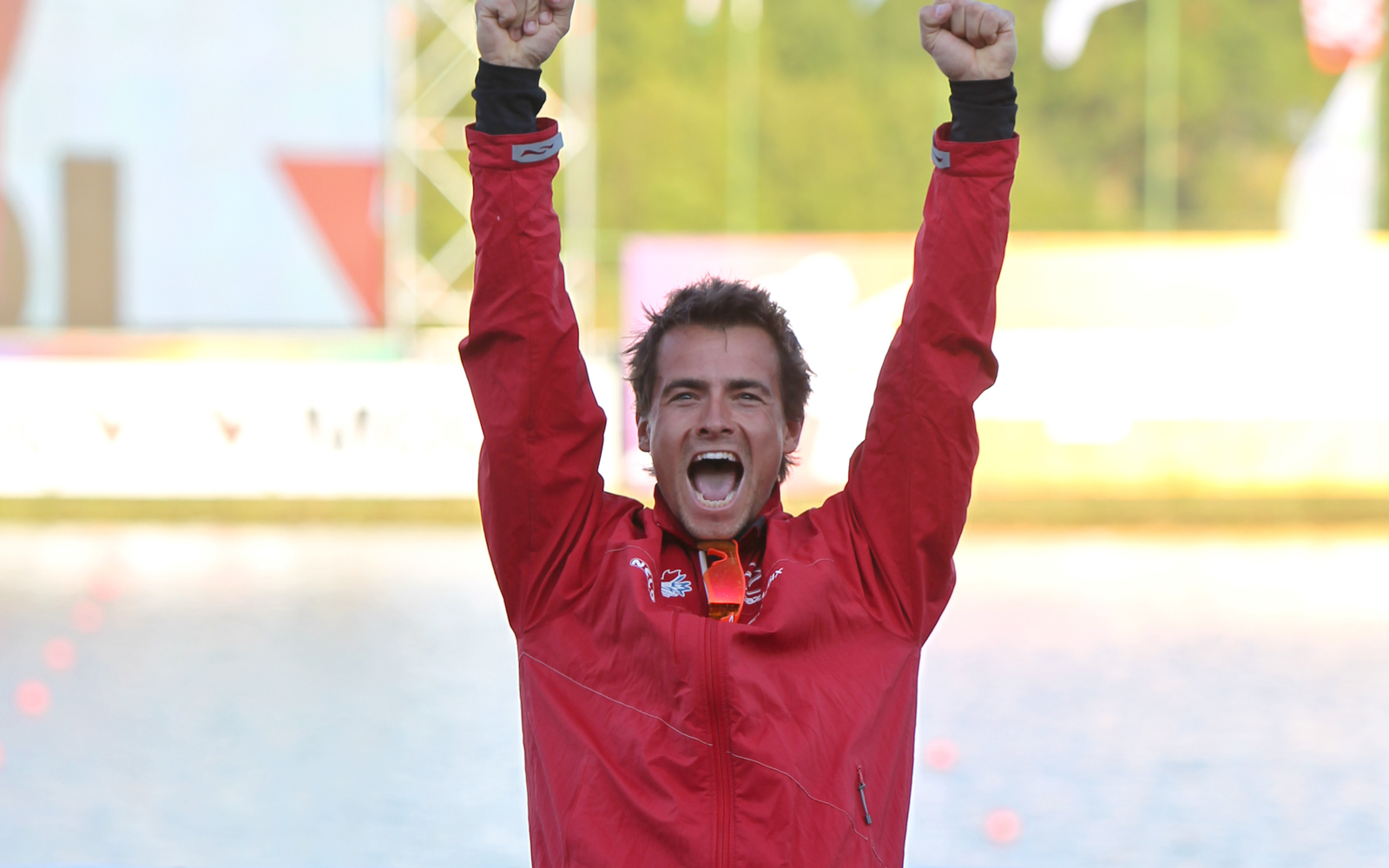 Un homme vêtu d'un manteau rouge et d'un pantalon noir, les bras levés, en train d'applaudir.