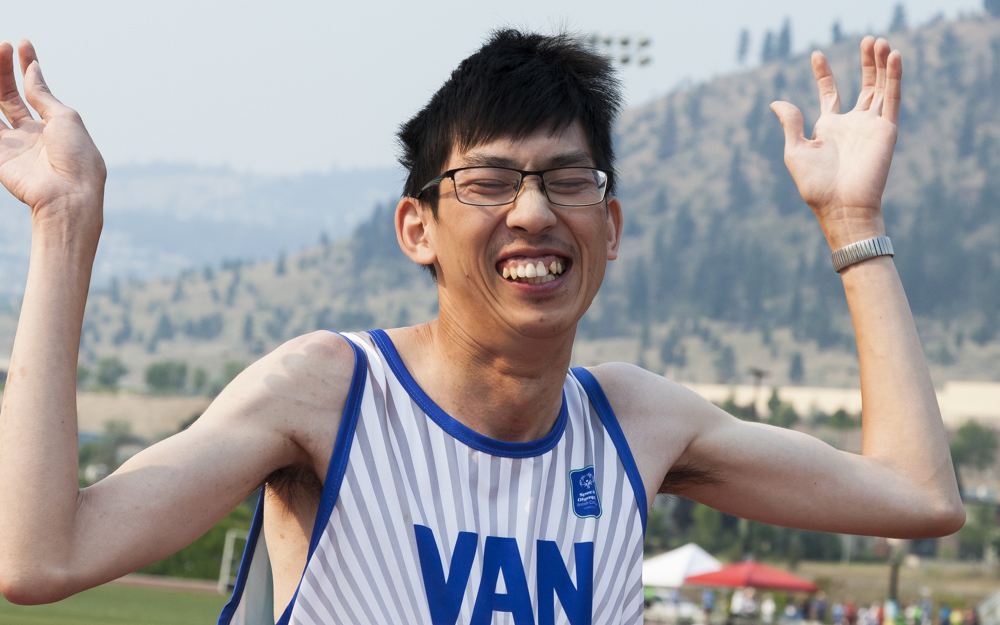 Special Olympics BC athlete with a proud smile throws his hands up in joy after his race.