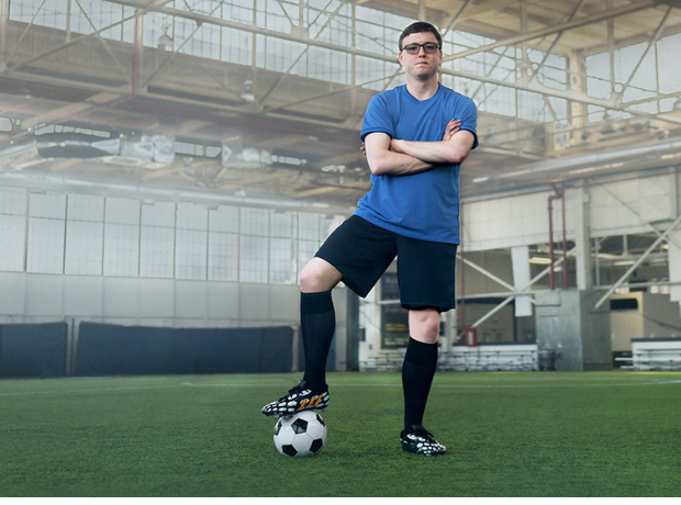 Soccer player standing with arms crossed and soccer ball beneath his foot.