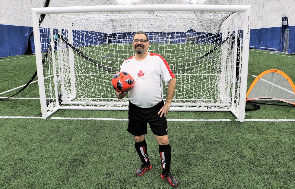 So Team Canada soccer player poses for a photo holding a soccer ball in front of a soccer net.