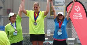 Kendall Salanski on top of podium raising hands with two other athletes