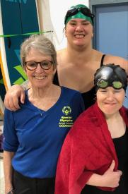 Judy smiling with two of her swimming athletes