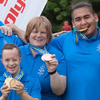 Sarah holding her medals up with two other athletes while smiling