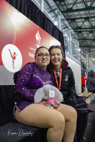 Figure skating athlete and coach sitting together and smiling.
