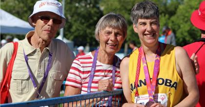 Brita at a Special Olympics event holding up her medal next to her parents.