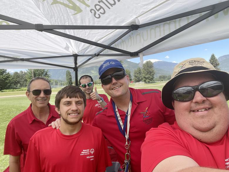 Athletes and coaches lean together and smile while standing under a tent