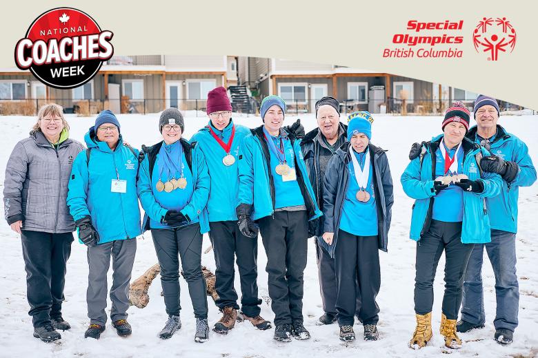 Special Olympics athletes wearing medals stand smiling beside their coaches outside on snowy ground