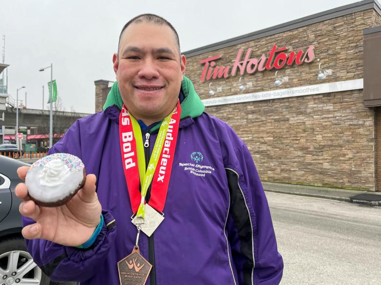 Athlete Vincent Li holding a Tim Hortons Special Olympics donut outside a Tim Hortons restaurant