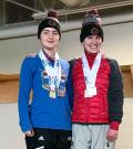 Madalyn, left, stands atop the podium smiling at the camera next to another athlete