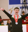 "Jordan Koughan lifts his arms up in victory with a big smile on the podium"