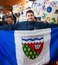 NWT speedskater Joshua Boudreau holds up the NWT flag in front of the Thunder Bay students whod rafted him, while holding support signs.