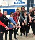 Steve Topham poses for a photo with Special Olympics rhythmic gymnasts as they all put their hands in to show off their bracelets.