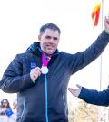 Ron raising one arm while holding his medal in the other