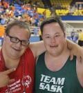 Two male Special Olympics athlete smile looking into the camera in front of a basketball court