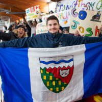 NWT speedskater Joshua Boudreau holds up the NWT flag in front of the Thunder Bay students whod rafted him, while holding support signs.