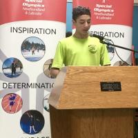 SONL Athlete Leader public speaking standing at a podium with Special Olympics banners in the background. 
