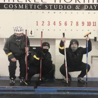 Curling athletes posing with their teammates and scoreboard