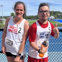 Two athletes smiling on the side of a track, one giving a thumbs up