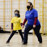 Active Start athlete and program leader holding hands while stretching their legs in a warmup