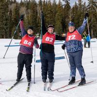 3 cross country skiers smiling holding their ski poles up