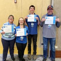 Four athletes smiling and holding certificates of achievement