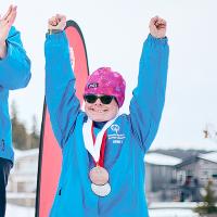 Ann smiling and holding both arms in the air on the podium