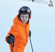 Wyatt poses for a photo on the ski hill in an orange snow suit.
