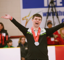 "Jordan Koughan lifts his arms up in victory with a big smile on the podium"